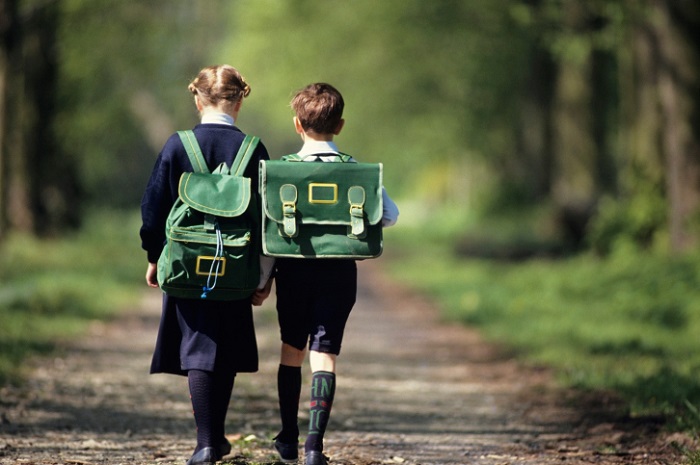 Boy (6-7) and girl (8-9) going school through forest, rear view